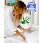 Load image into Gallery viewer, A blond woman holding a bottle of pillow mist bends over a bed to spray the pillows.