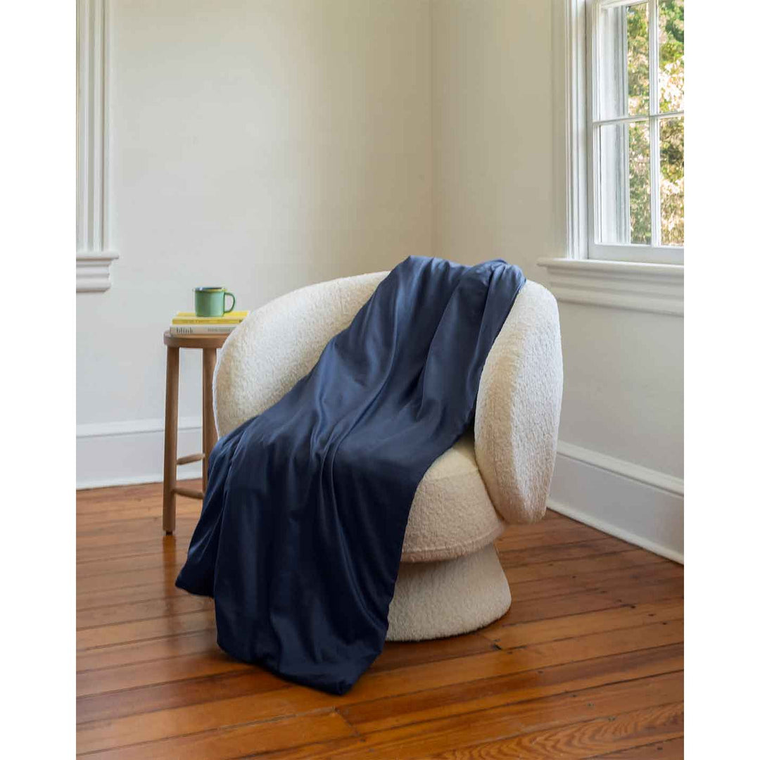 A cotton duvet cover on a weighted blanket on a white chair next to a stack of books and green window [44422682083547, 45027100033243]