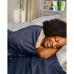 Load image into Gallery viewer, A smiling woman with eyes closed wrapped in a weighted blanket with luna blue cover resting in bed [44422682083547, 45027100033243]
