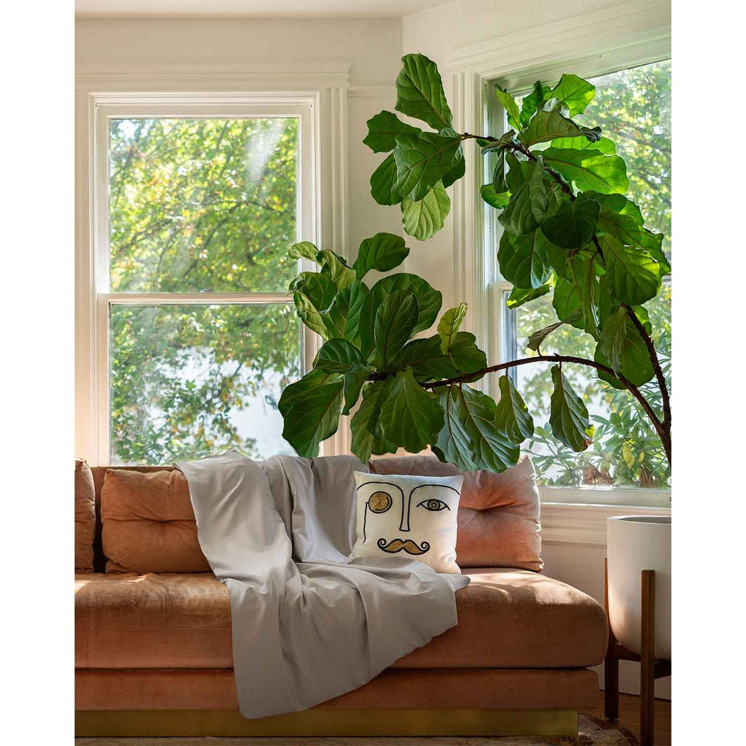 A silver sage duvet cover on a pink sofa next to a large plant and a fun throw pillow [44422682050779, 45027099771099]