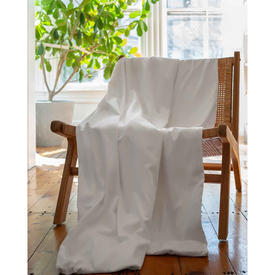 A white cotton duvet cover on a chair in front of a green plant inside a living room [44422681886939, 45027099410651]