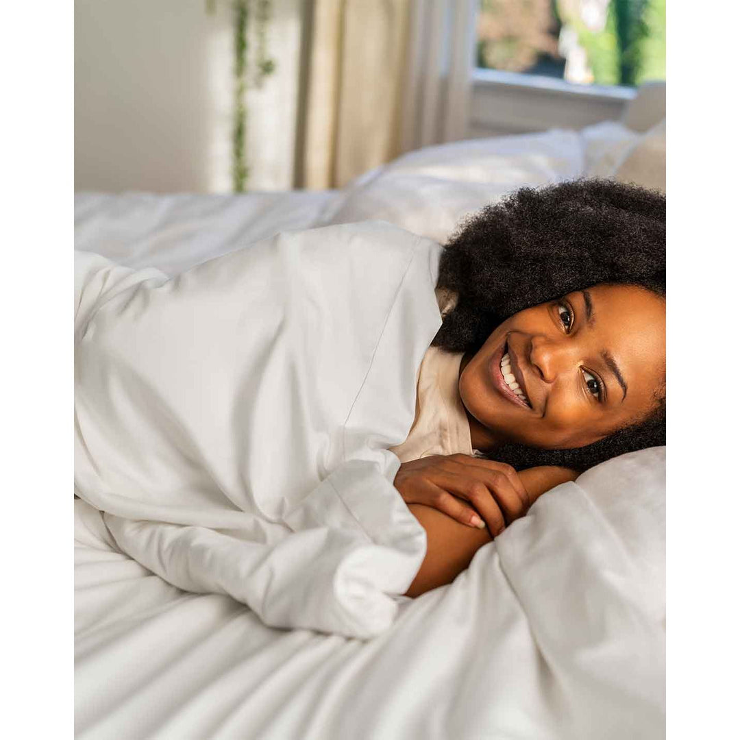 A smiling woman in bed wrapped in a cotton blanket and duvet [44422681886939, 45027099410651]