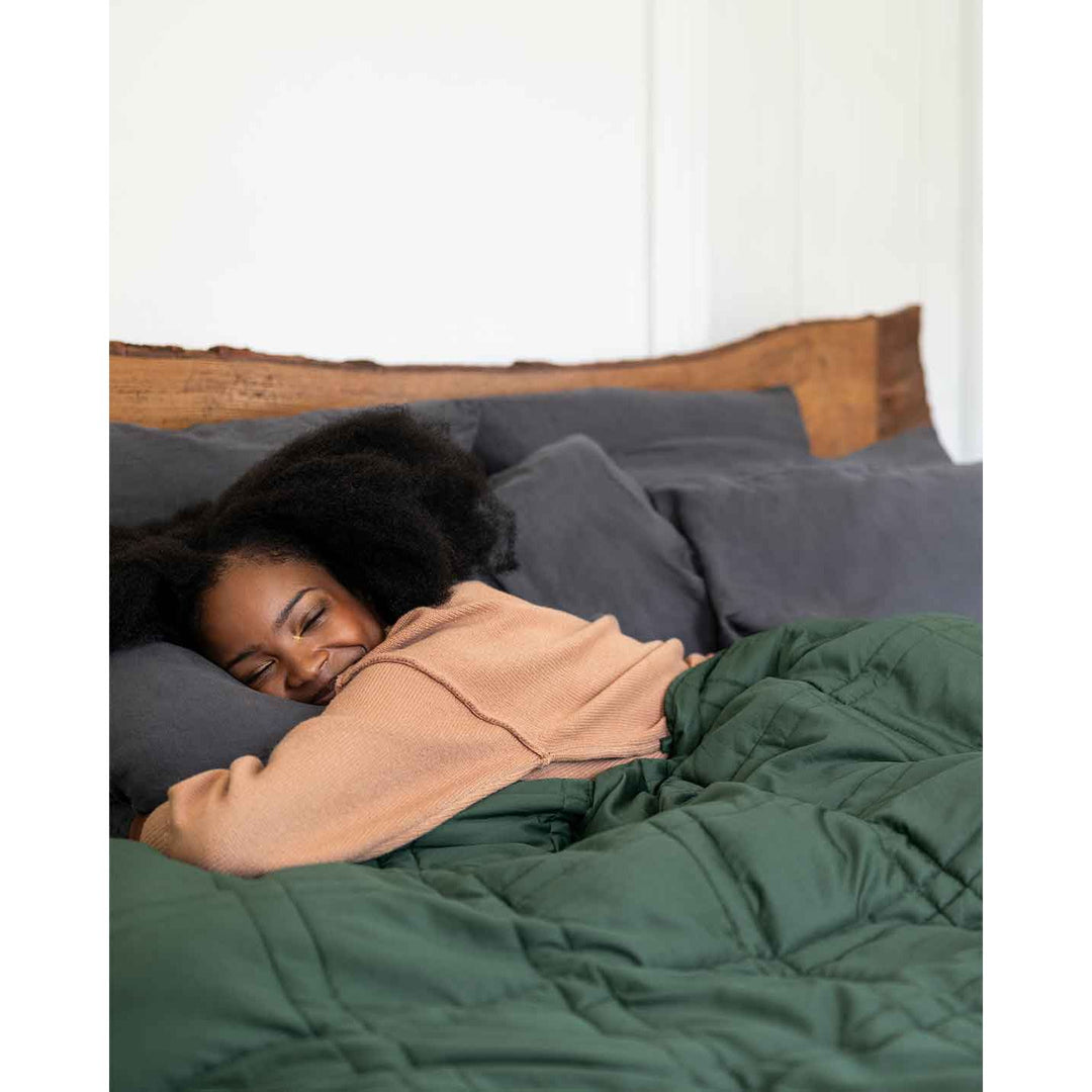 A woman smiles with eyes closed, hugging a pillow under a spruce green weighted blanket [44422820561115, 44422814826715, 44422813090011, 44422818234587]