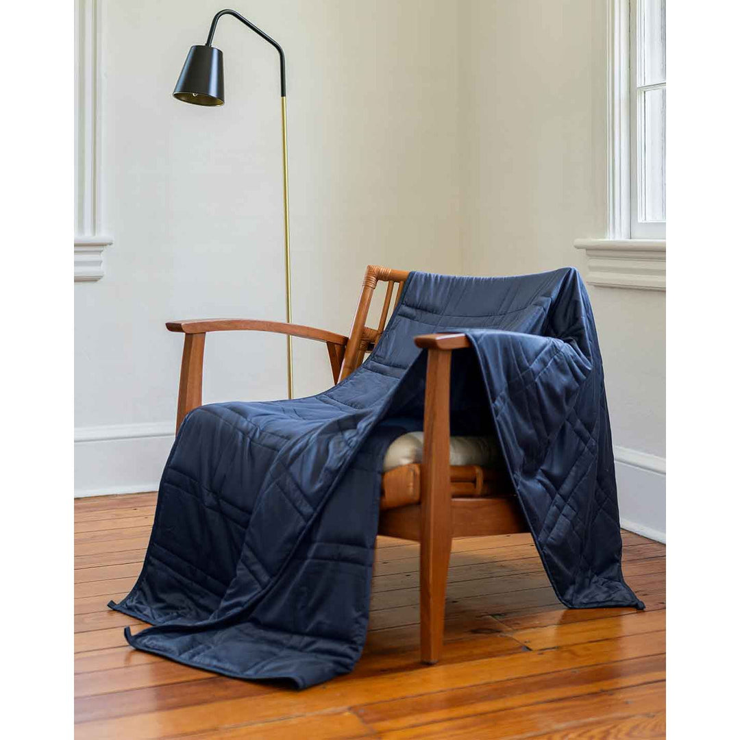 A blue weighted blanket across a chair next to a lamp. [43649942782171, 44422804340955, 44422811287771, 44422816432347,45574417875163, 45574418137307, 45574418170075, 45574418268379]