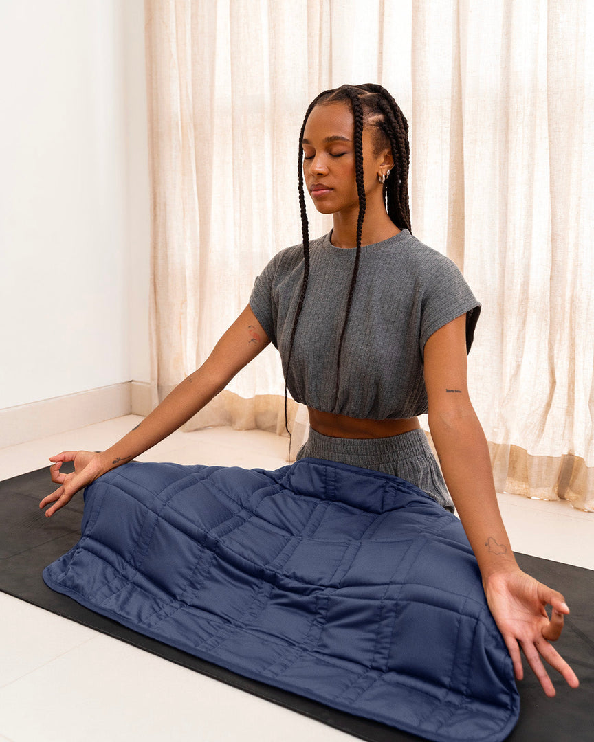 A young woman with braided hair sits cross legged on a yoga mat with her eyes closed. She has a luna blue lap blanket across her lap while she meditates. [43580656713947, 46288037380315, 46730820911323, 46730820944091, 46730820976859, 46730821009627]