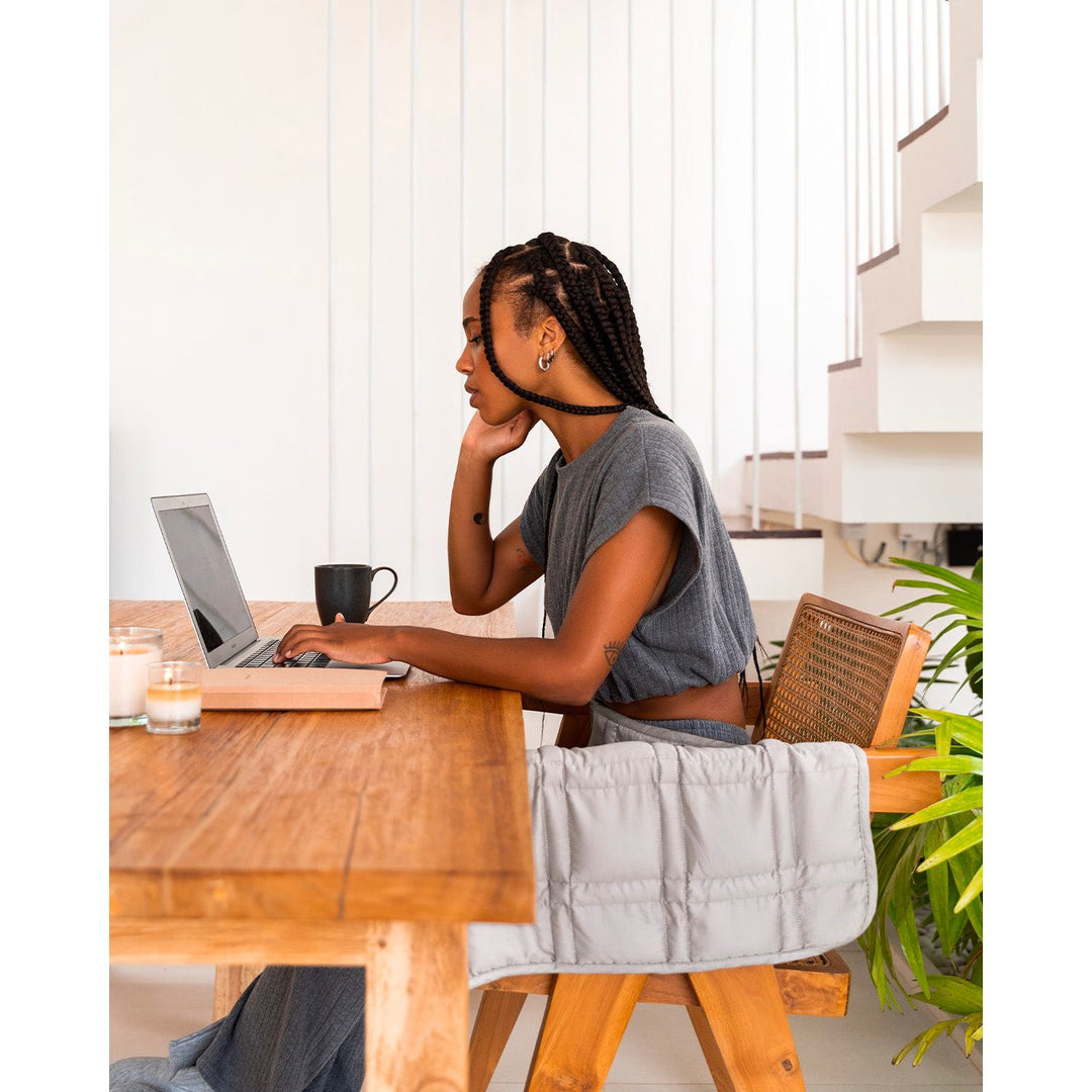 A young woman with braids sits at a table working on a computer, with a silver sage lap blanket. [43580656746715, 46288037413083]