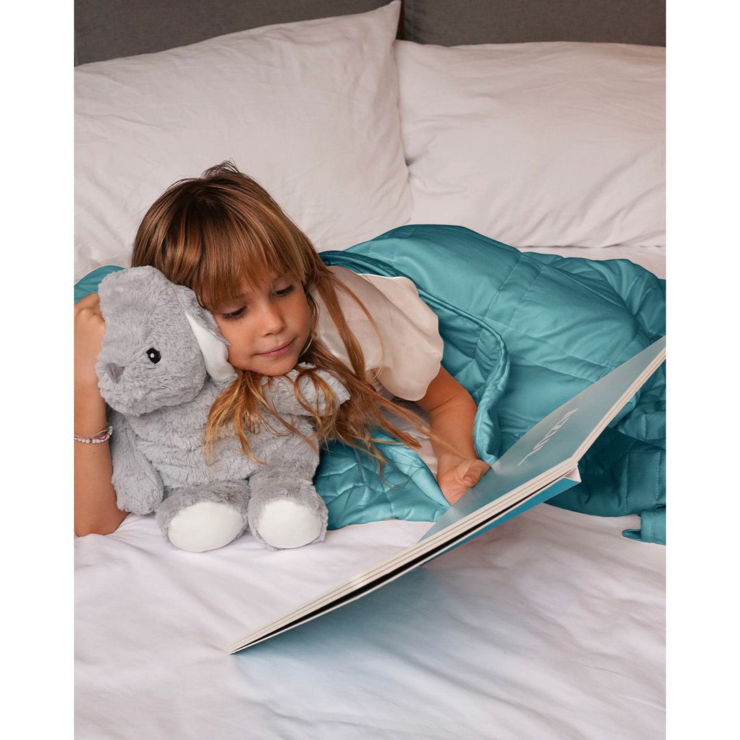 a little girl reads in bed with her stuffed animal under a weighted blanket [44385363689691]