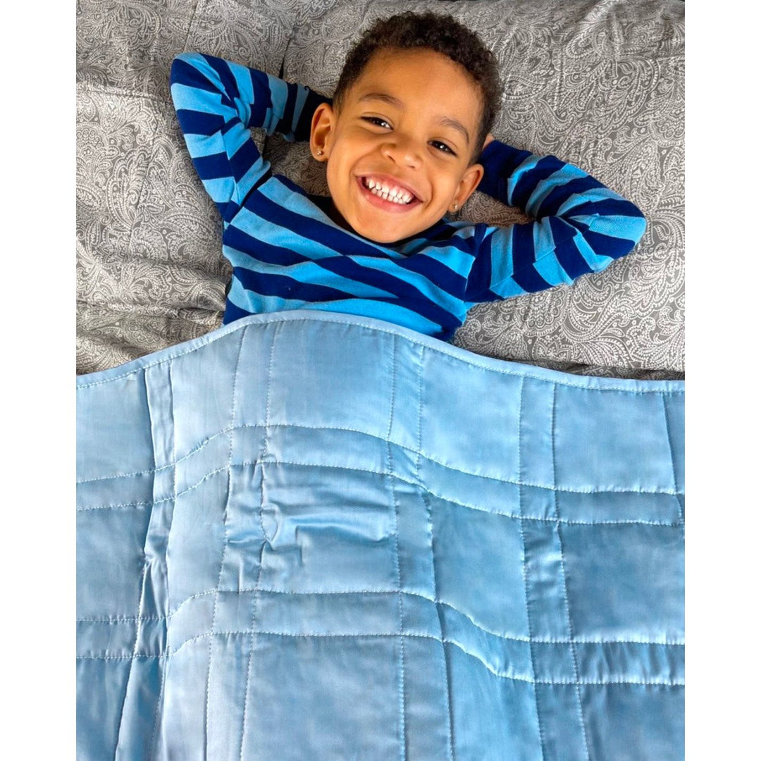 A boy smiles at the camera wearing an indigo weighted blanket [37958770163896]