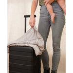 Load image into Gallery viewer, A woman holding a baby next to a suitcase, with a lap blanket in one hand [43936127221979]
