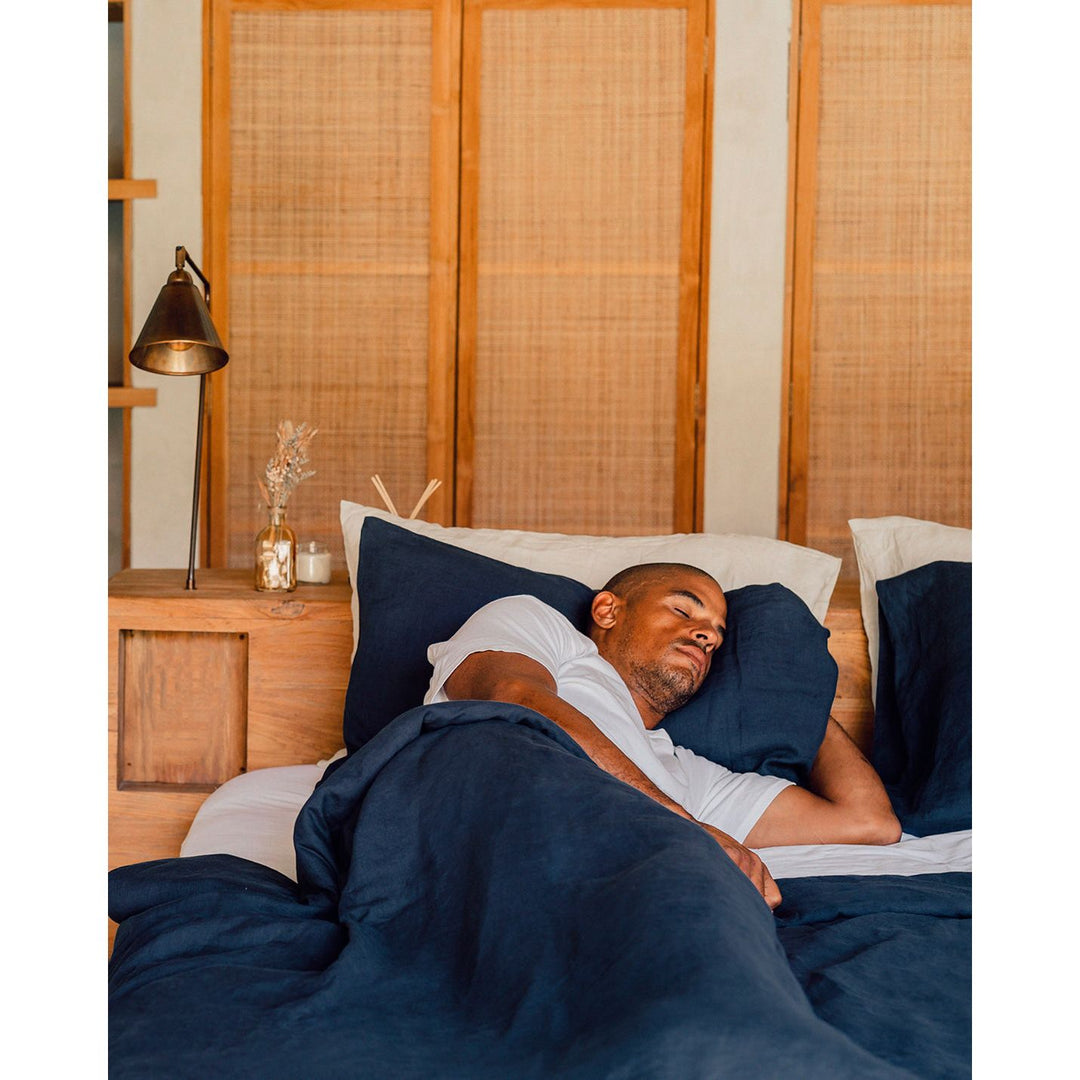 A man sleeping in bed with a navy linen duvet cover and pillows. [32783545565264, 32783545172048]