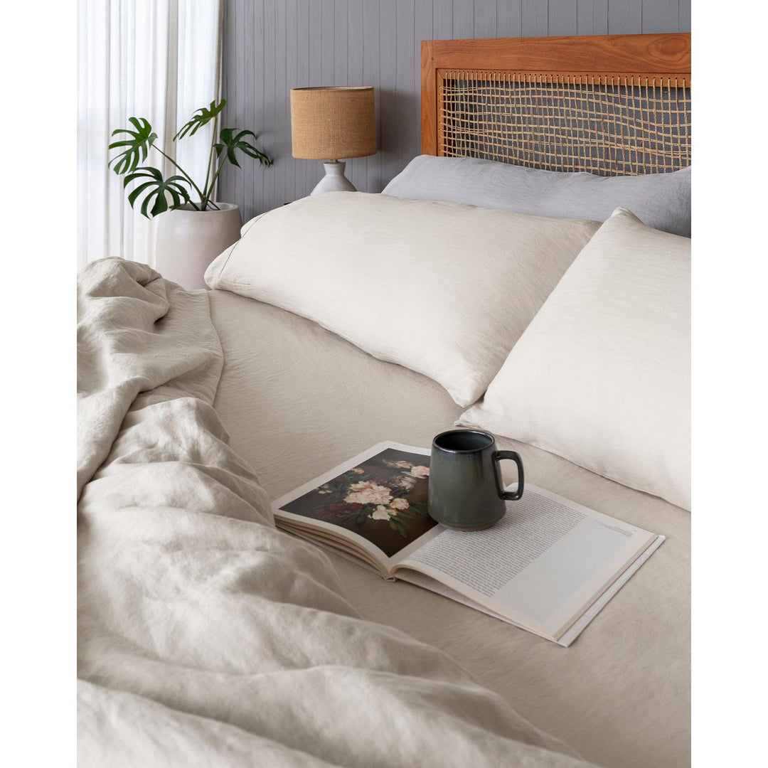 A bed with king size pillowcases in oatmeal linen and dove grey, a magazine and a mug. [32783545729104, 32783545335888, 32783545532496, 32854359507024, 32854401843280]