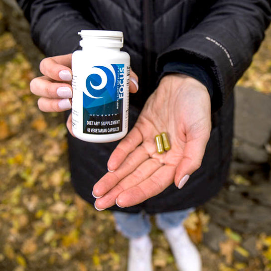 Female holding a bottle of New Earth's Focus in one hand and two capsules of the same product in the other.