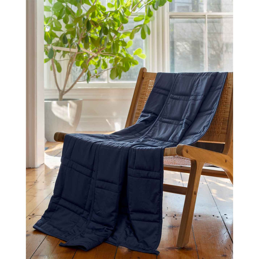 A soft cotton weighted blanket the color luna blue is draped across a chair in a home. [43649942782171,46089486074075]