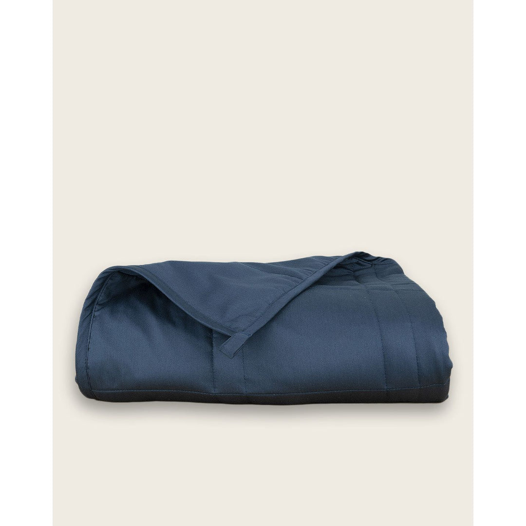 A blue cotton weighted blanket folded up on a plain background. [44385233109211,46089486074075]