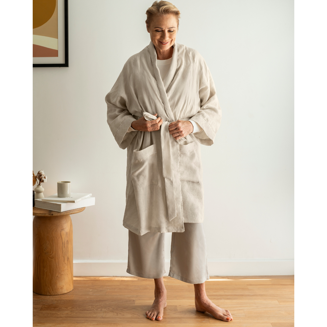 Older woman tying oatmeal linen robe 
[45949480796379, 45949488070875]