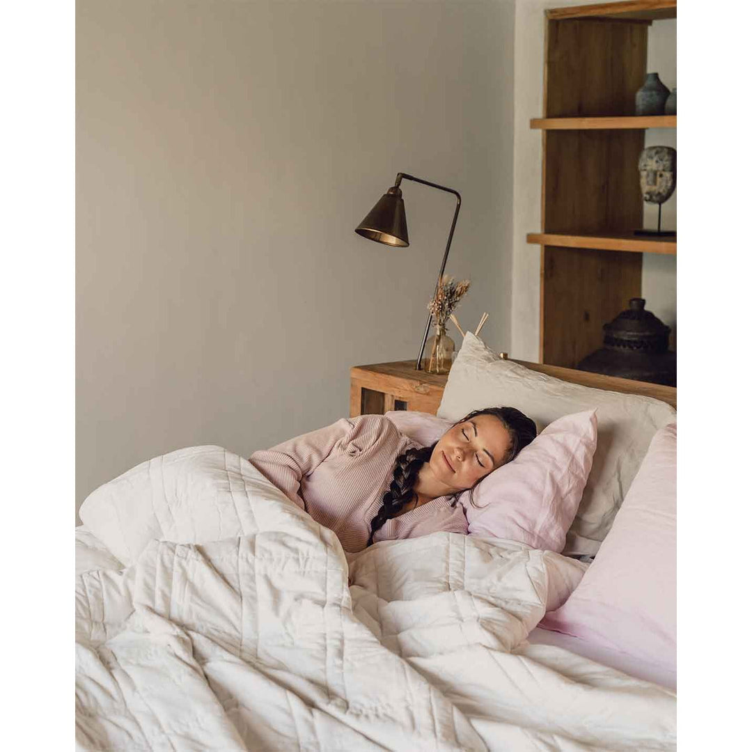 A young woman with a braid sleeps peacefully in a bed with a pink pillowcase and a white weighted blanket across her body.  [42934587818203,42934587850971, 42934587883739]