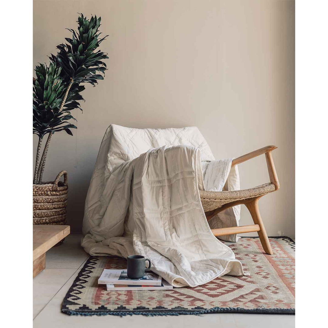 A luxurious looking white cotton weighted blanket drapes across a chair, next to a coffee mug on the floor and a plant. [44385233141979, 44385233207515]