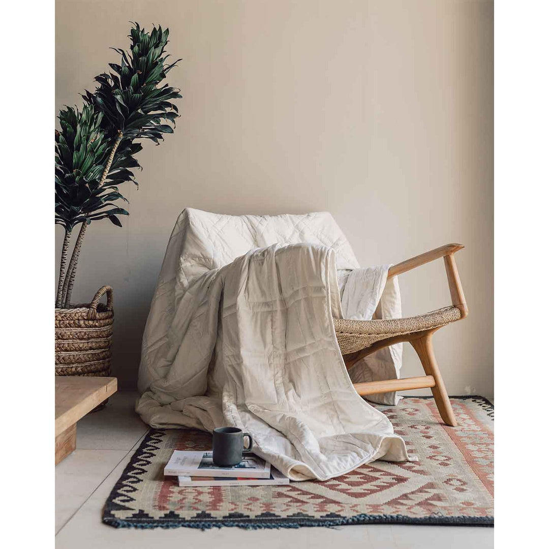 A luxurious looking white cotton weighted blanket drapes across a chair, next to a coffee mug on the floor and a plant. [42934587818203, 45574417940699, 42934587850971, 46452818444507]