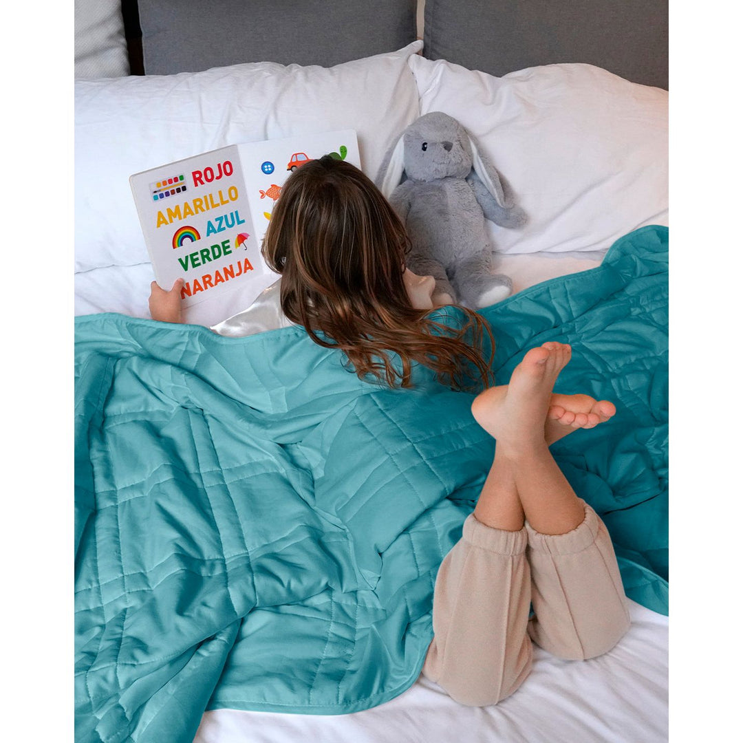 a little girl reads in bed with aqua mini weighted blanket [44385363689691]