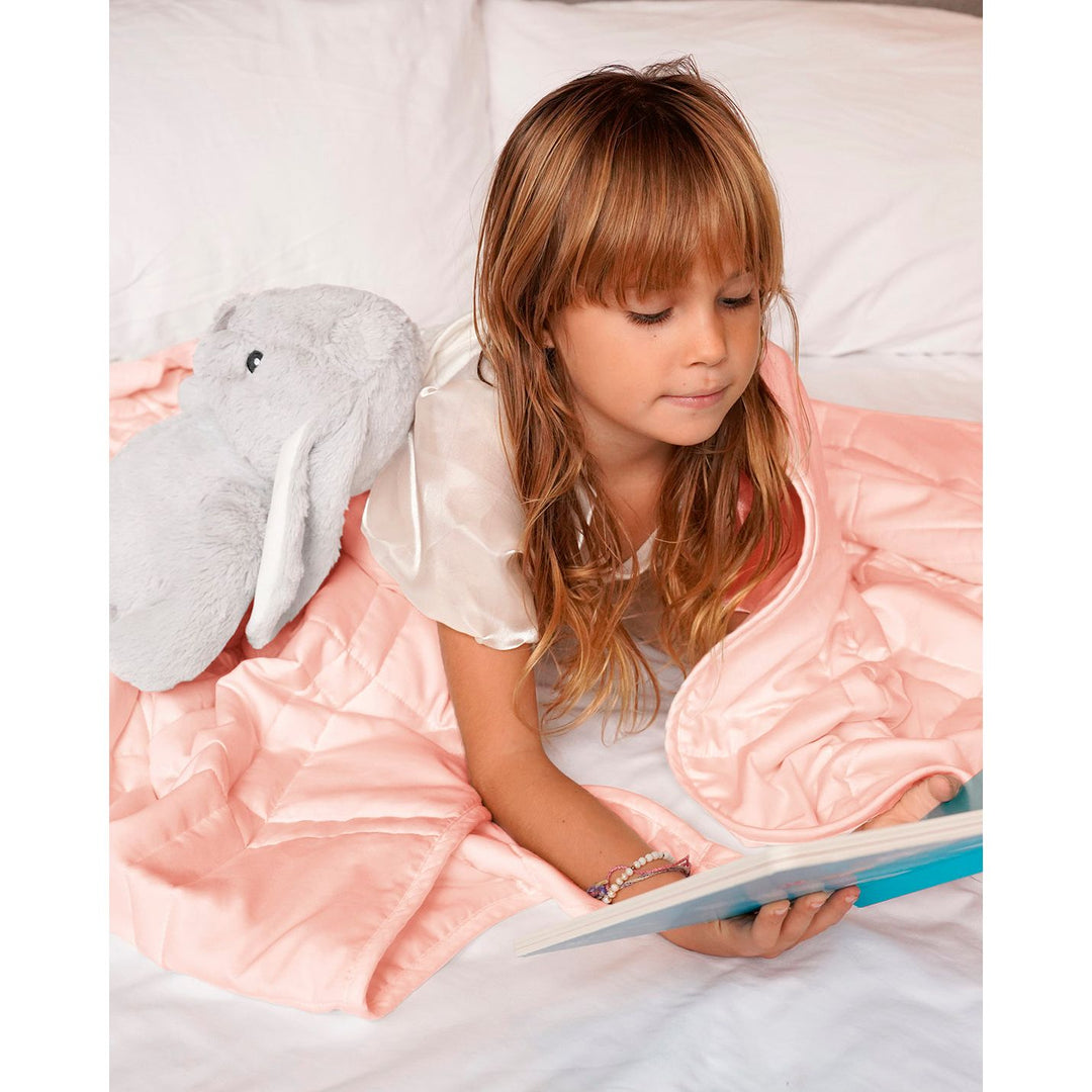 a little girl reads a book with her stuffed animal under a weighted blanket [44385363656923]