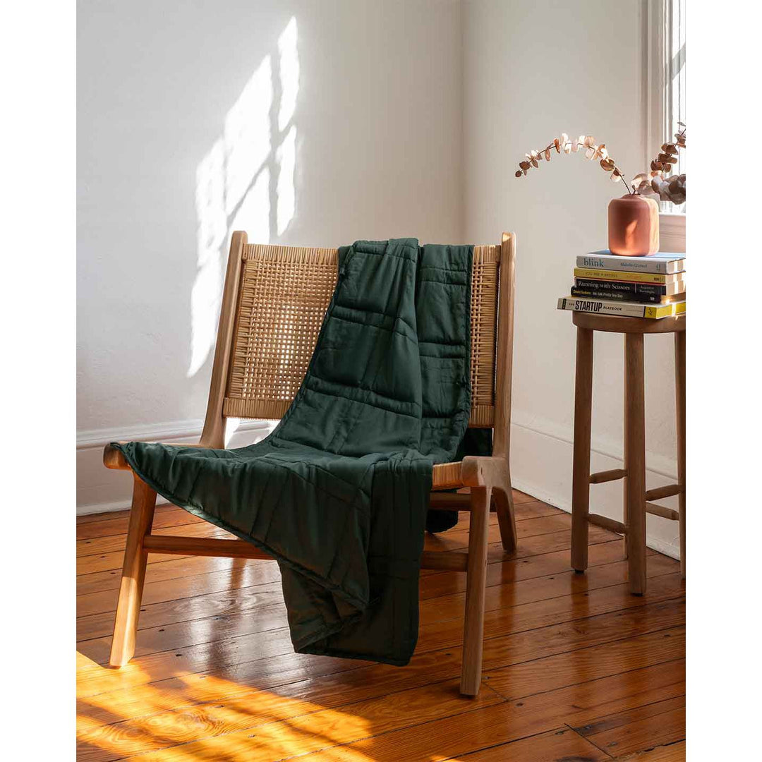 A weighted blanket tossed over a chair next to a stack of books [44422820561115]