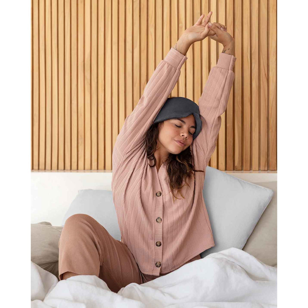 A young woman reaches up stretching wearing a silk sleep mask on her head [44377020793051]